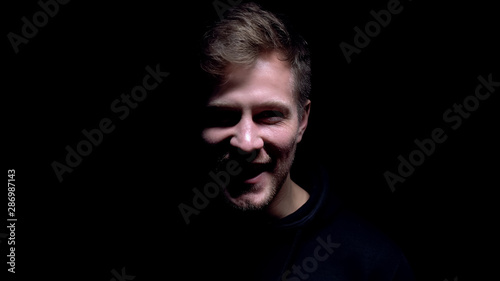 Crazy man laughing and staring into camera on black background, insane criminal