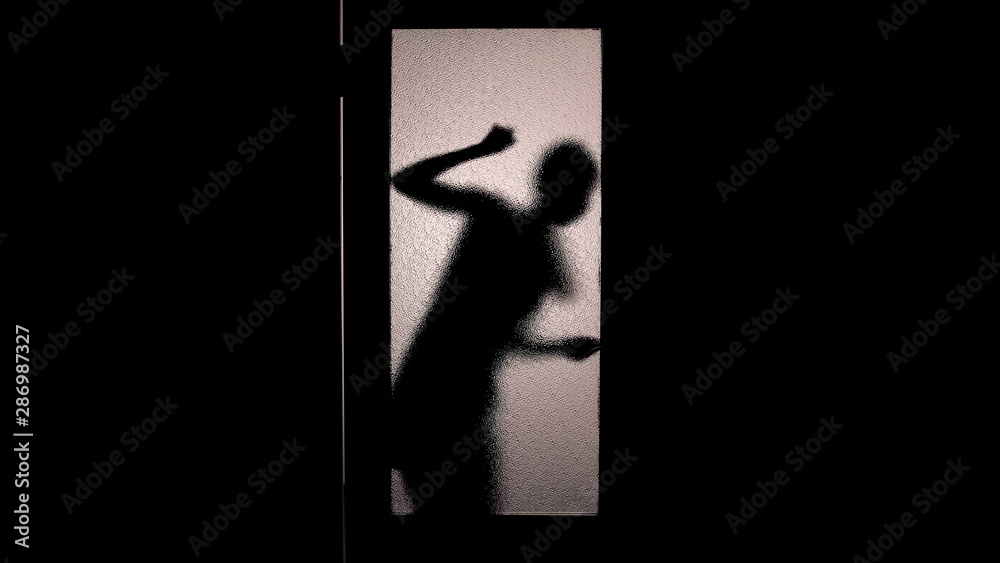 Silhouette of scared woman knocking at glass door checking handle, fear, escape