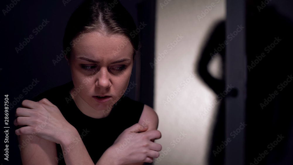 © motortion - Scared kidnapping victim looking at male silhouette entering room, mistreatment