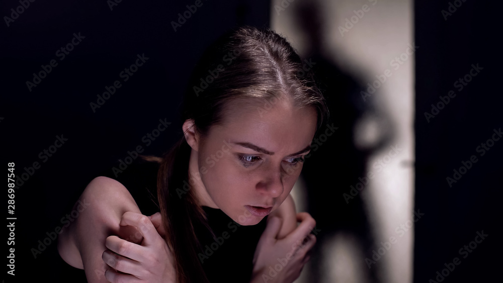 Scared crying woman sitting alone in room, cruel tyrant husband shadow outside Scared crying woman sitting alone in room, cruel tyrant husband shadow outside