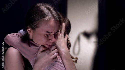 Fotografia Scared woman hugging daughter, frightened by cruel man with belt entering room