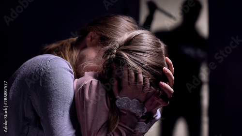 Daughter and mother watching crazy maniac with knife shadow outside door, fear photo