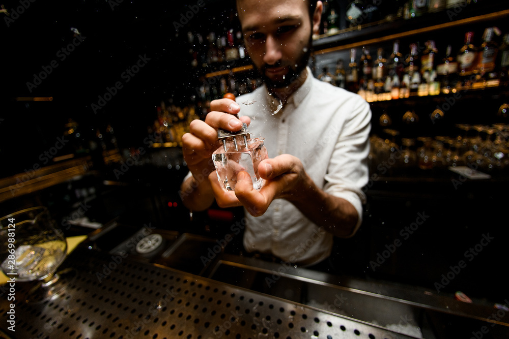 Fish-eye shot male bartender crushing ice cube with a special instrument