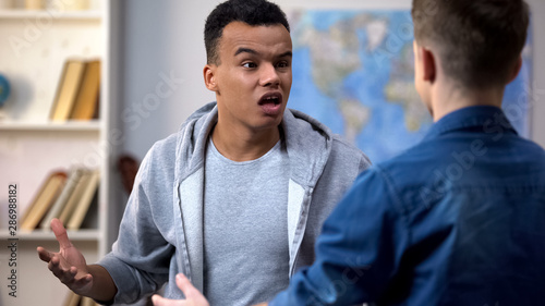 Fotografie Aggressive multiracial teenagers having conflict, racial discrimination, quarrel