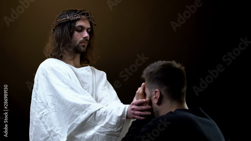 Son of God supporting crying desperate man on dark background, spiritual help