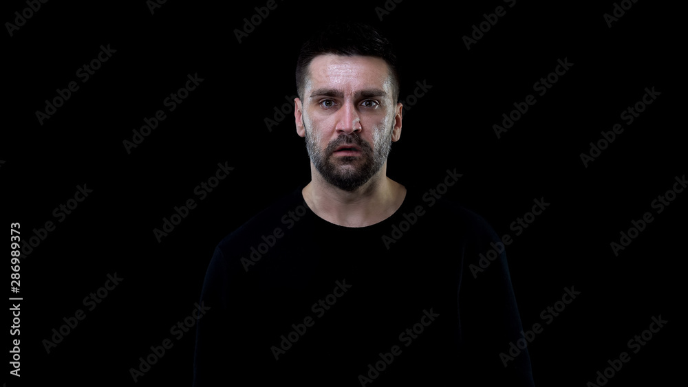 Scared male looking camera on black background, nightmare horror, shock stress