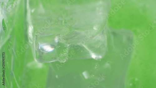 green cocktail is poured into a glass. there are cubes of cold ice. The drink drips and bubbles and splashes. macro mode. Angle from above. the beginning of a fun party. studio lighting.