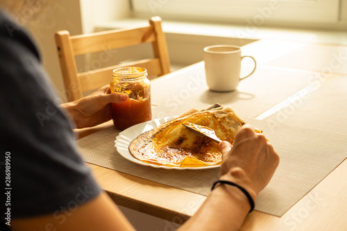Woman adding apricots jam on homemade pancakes in the morning.