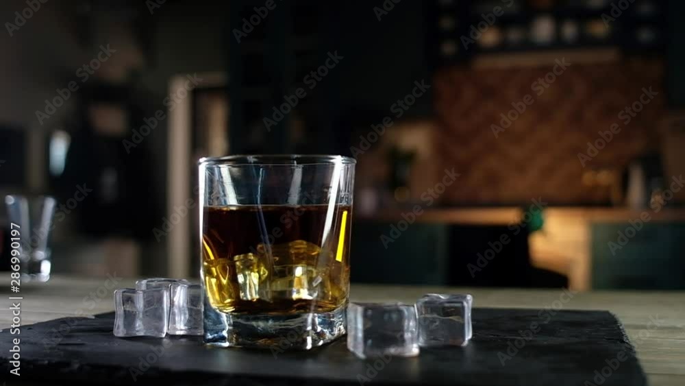 panoramic shot of a clear glass of strong single malt whiskey with a large ice cube. The glass is on a black stand. Lay next to the ice crystals. Festive alcoholic drink for connoisseurs. panoramic shot of a clear glass of strong single malt whiskey with a large ice cube. The glass is on a black stand. Lay next to the ice crystals. Festive alcoholic drink for connoisseurs.