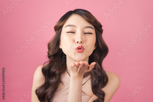 Beautiful young Asian woman blow a kiss on pink background