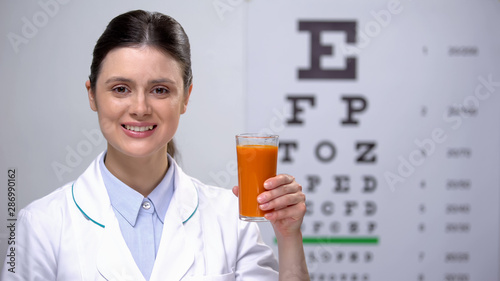 Oculist holding glass with carrot juice, organic drink for vision, eyesight care