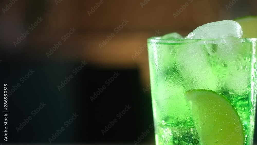 in wet glass clear glass with drops of water poured green cocktail with large cubes of cold ice. slice of fresh lime was placed on rim of the glass. Panoramic shooting of Festive drink for new year in wet glass clear glass with drops of water poured green cocktail with large cubes of cold ice. slice of fresh lime was placed on rim of the glass. Panoramic shooting of Festive drink for new year