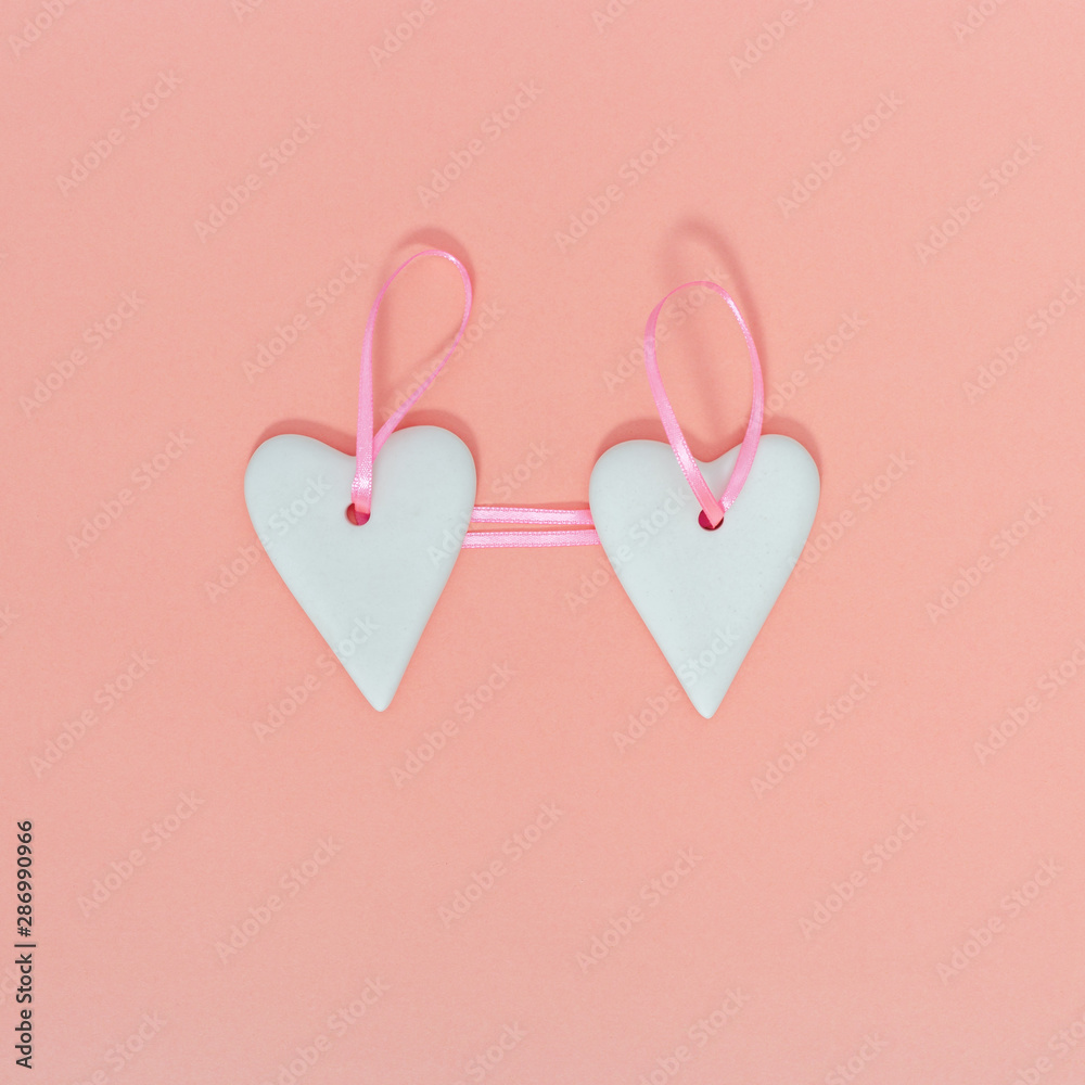 Valentine greeting concept. Two lovely white heart hanging on pink ribbon on paper background of pastel pink.