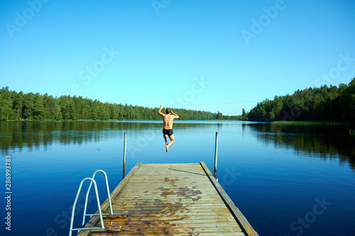 Mann springt vom Holzsteg in See mit Wald im Hintergrund