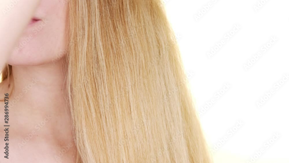 In slow motion, against a white studio background, a young blonde woman brushes her hair gently In slow motion, against a white studio background, a young blonde woman brushes her hair gently