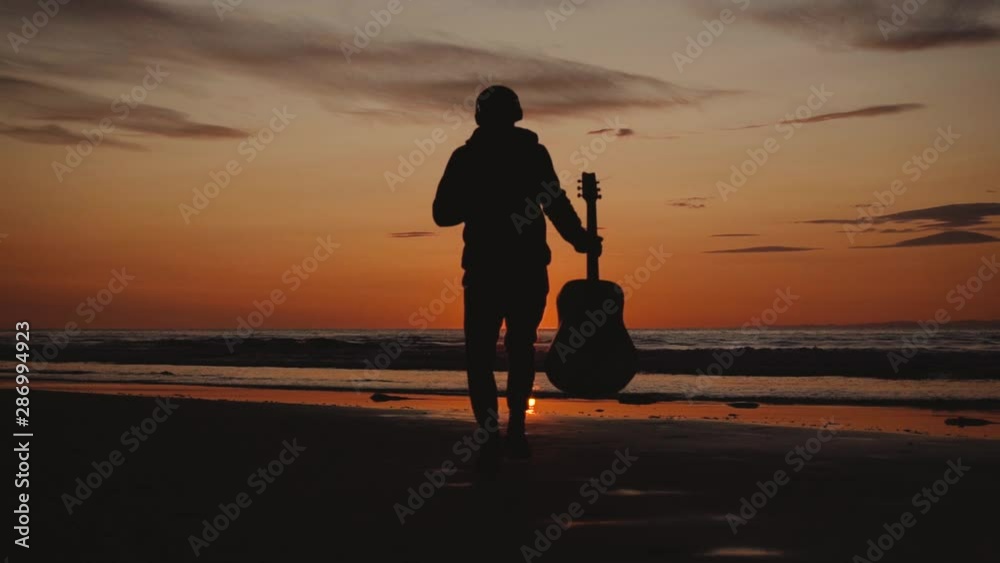 Man running with guitar in back sand beach at sunset. Beautiful, moody shots from the Sony a7iii. Man running with guitar in back sand beach at sunset. Beautiful, moody shots from the Sony a7iii.