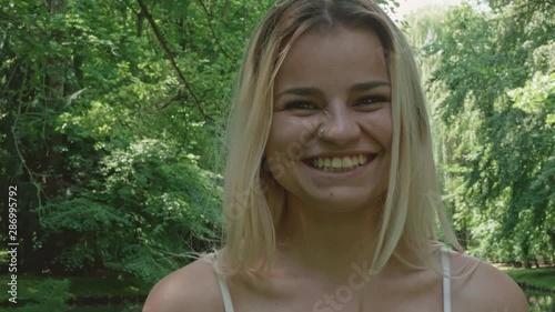 A young blonde woman in a forest stands facing the camera, giggling maniacally