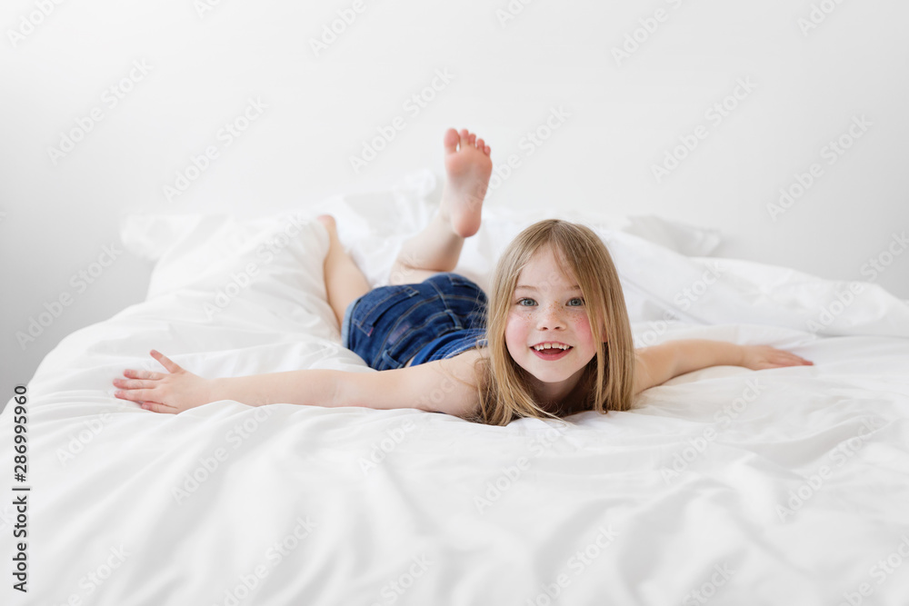 © Lisa Tichané - Smiling young girl lying on bed with arms extended © Lisa Tichané - Smiling young girl lying on bed with arms extended