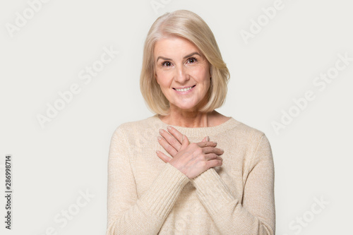 Grateful senior woman with hands on chest feel thankful