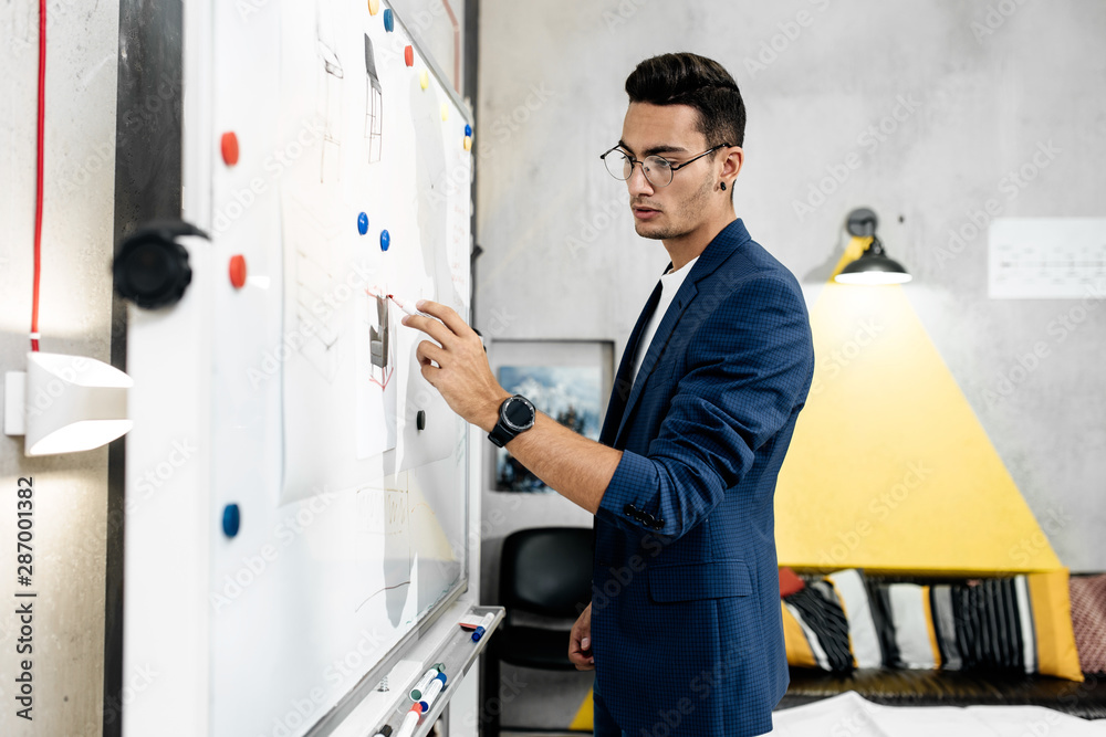 Fototapeta premium The architect dressed in blue checkered jacket attaches blueprints to a magnetic board on the wall in the office