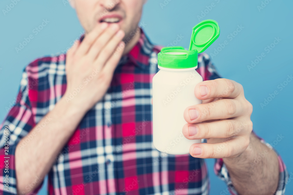 Sad man shows a container of medicine, copy space, advertising, text. Cropped image, closeup, blue, background Sad man shows a container of medicine, copy space, advertising, text. Cropped image, closeup, blue, background