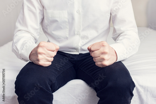 Angry man sitting on the bed and waiting for someone, man's hands and fists, cropped image, close-up, toned