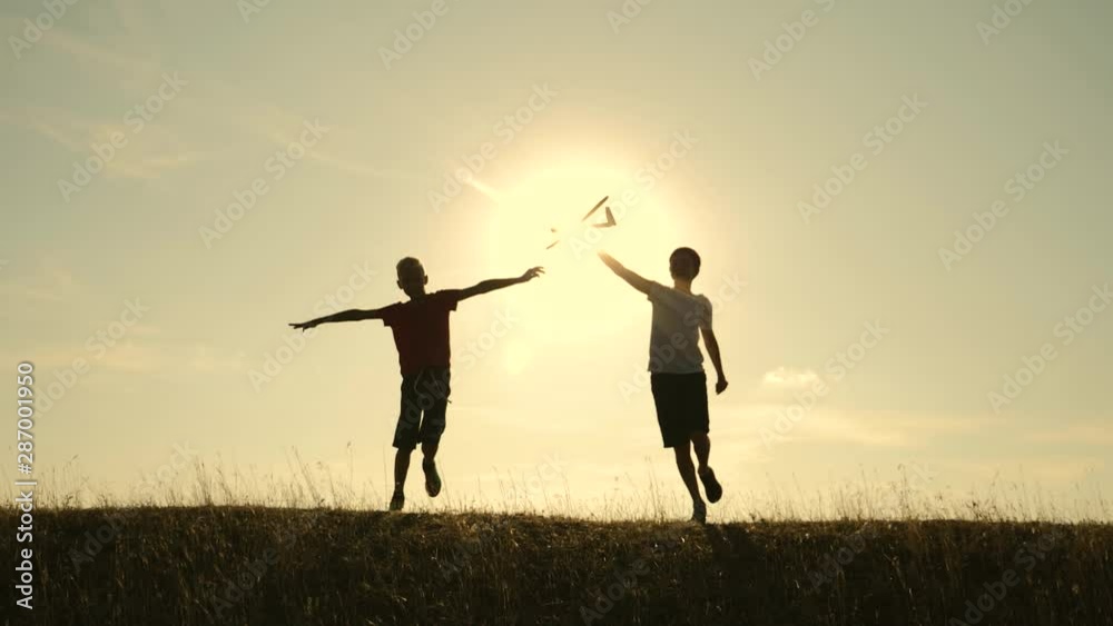 Two boys play with a wooden plane at sunset. Silhouette of children playing with an airplane. Dreams of flying. Children concept. Teamwork. Games and teamwork Two boys play with a wooden plane at sunset. Silhouette of children playing with an airplane. Dreams of flying. Children concept. Teamwork. Games and teamwork