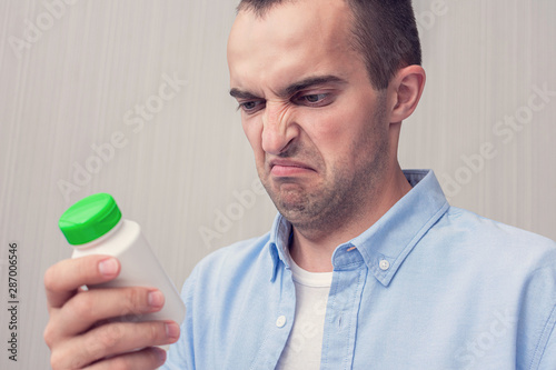Dissatisfied man with a medicine in his hands, man does not want to take pills, toned