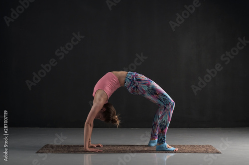 Sporty young woman practices yoga asana chakrasana or urdva dhanurasana or wheel pose. Studio full length shot photo