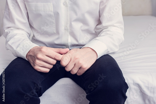 Male sits on the bed, a man doubts, man's hands, cropped image, closeup, toned