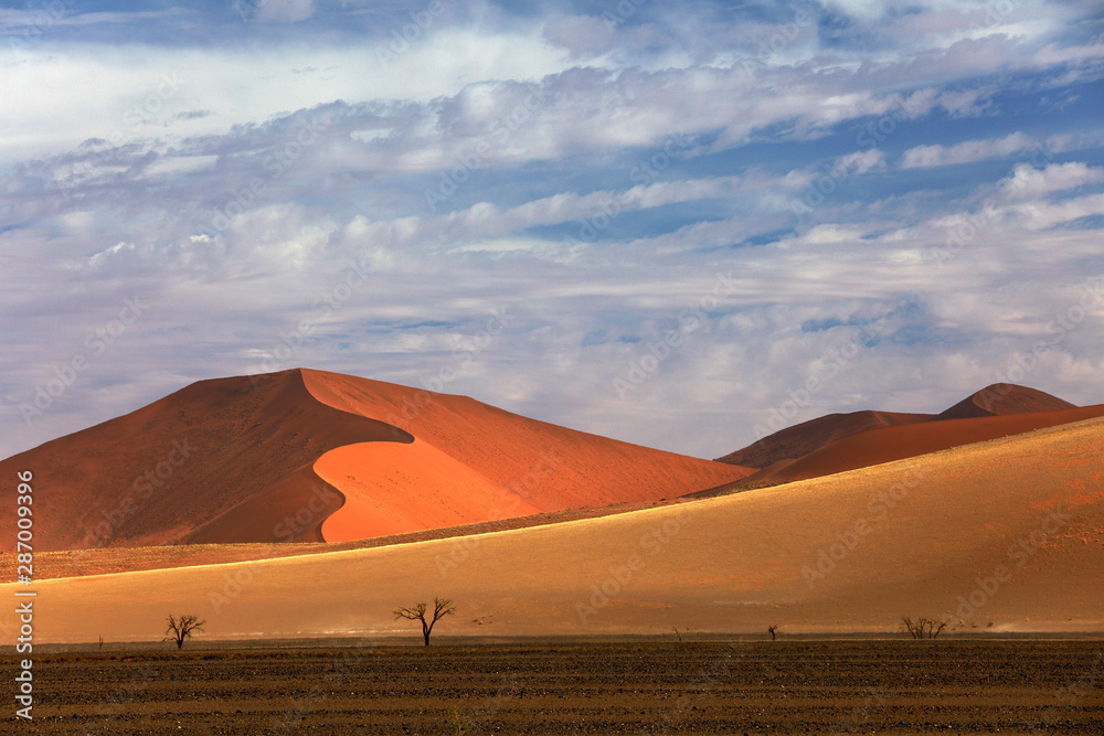 Namibia landscape. Big orange dune with blue sky and clouds, Sossusvlei, Namib desert, Namibia, Southern Africa. Red sand, biggest dune in the world. Travelling in Africa.