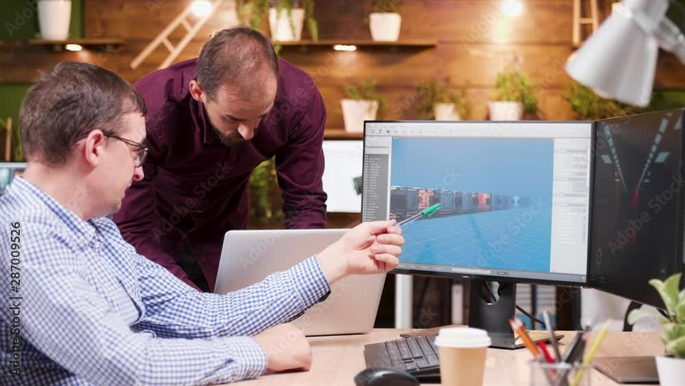 Graphic designer in game industry sitting at his office showing his assistant new gaming graphics. Graphic designer in game industry sitting at his office showing his assistant new gaming graphics.