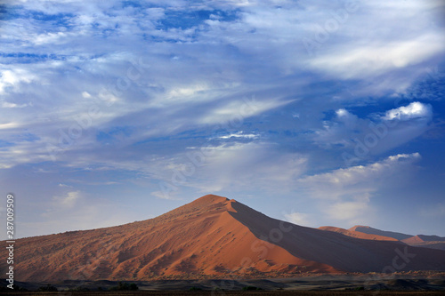 Namibia landscape. Big orange dune with blue sky and clouds, Sossusvlei, Namib desert, Namibia, Southern Africa. Red sand, biggest dune in the world. Travelling in Africa.