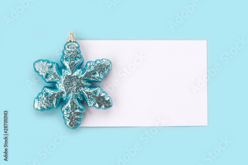 White paper card decorated with snowflakes on light blue background. New Year, Christmas and winter concept. Flat lay, top view, free copy space. © evso