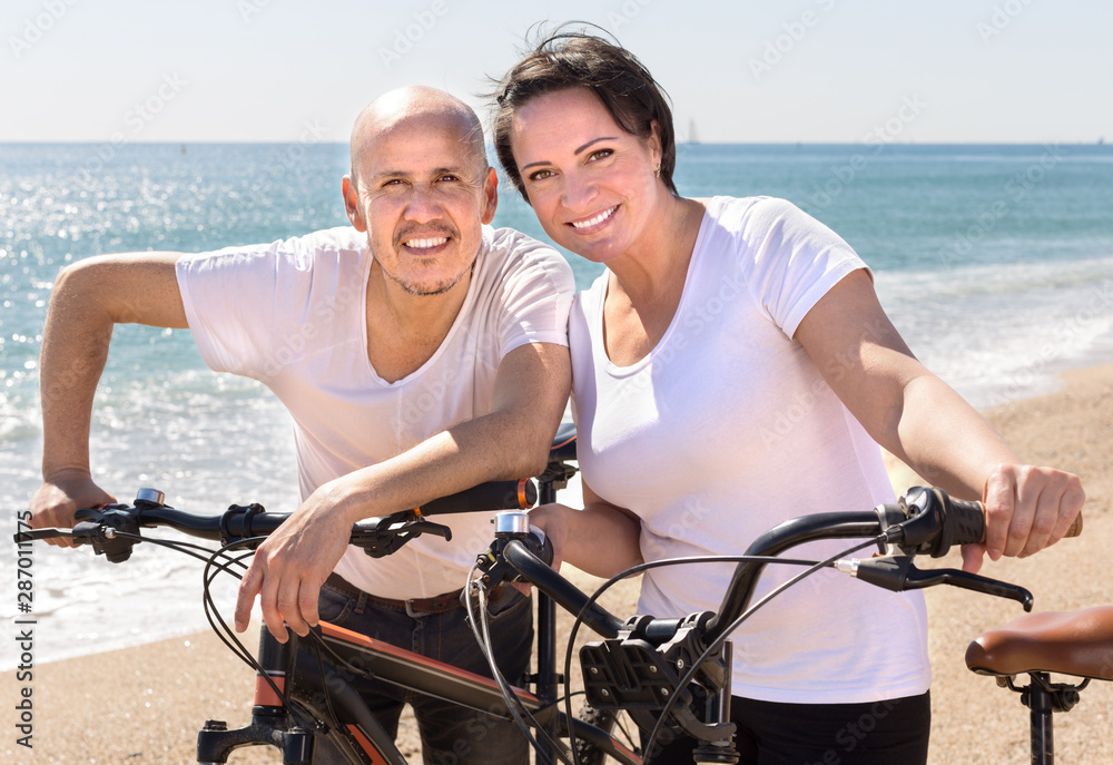 middle-aged man and woman with bicycles walking on the beach
