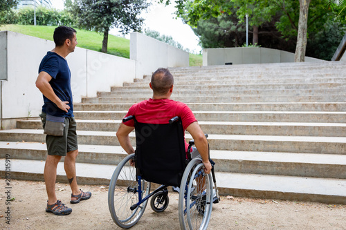 Person in a wheelchair with an assistant in front of a stair.
