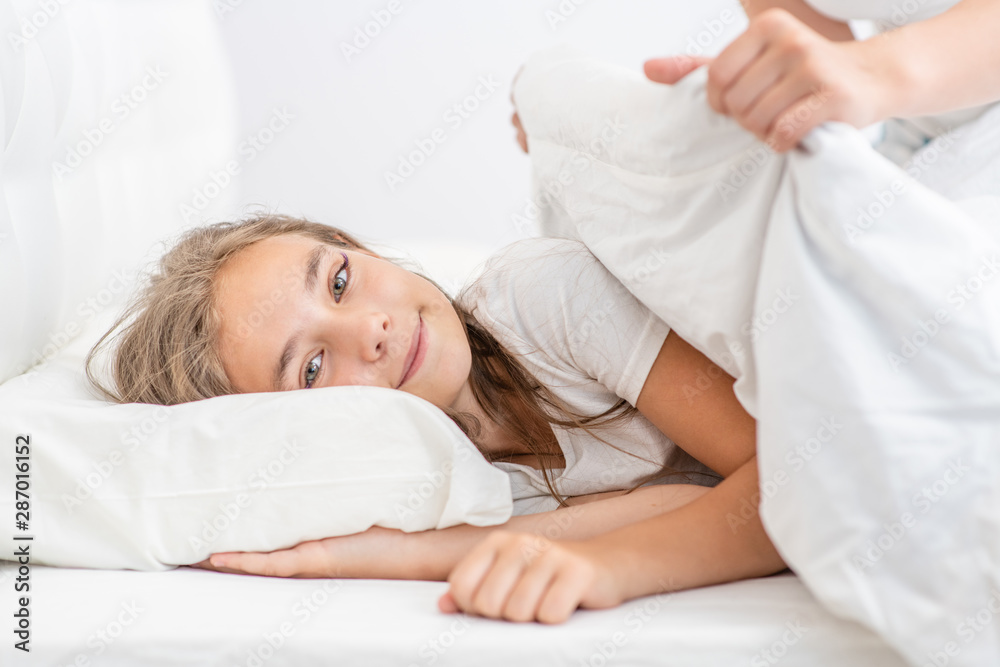 Smiling girl is covered by a caring mother before bedtime Smiling girl is covered by a caring mother before bedtime