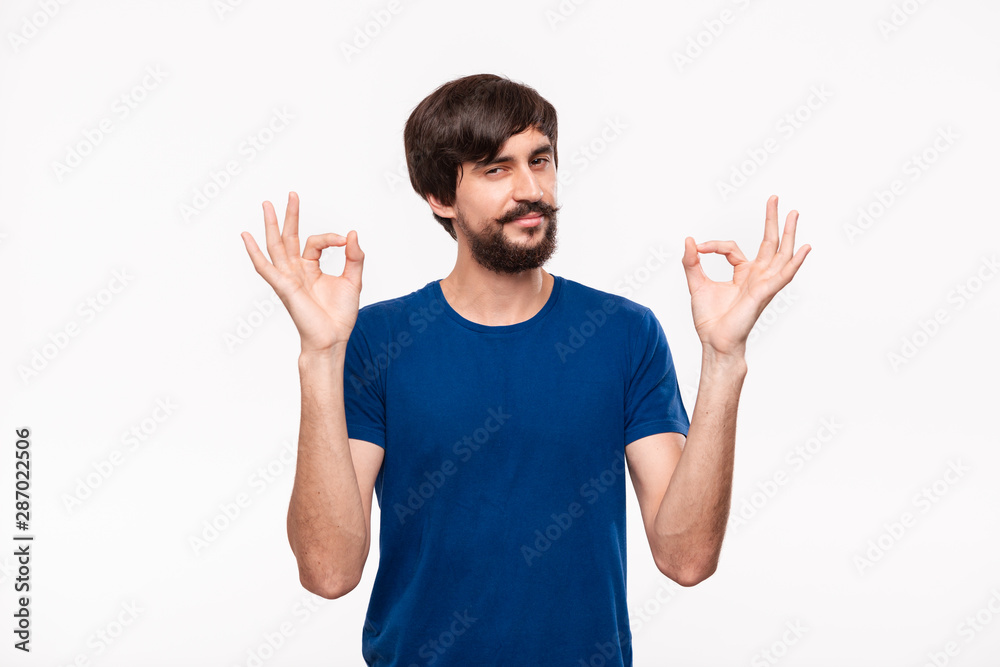 Handsome brunet bearded man with mustaches in a blue shirt showing gesture of OK sign with two hands standing isolated over white background. Handsome brunet bearded man with mustaches in a blue shirt showing gesture of OK sign with two hands standing isolated over white background.