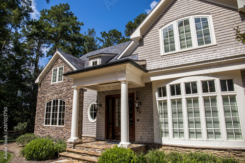 Front view of large estate home in the south with a gravel driveway and lots of windows. house made of brick  stone and clapboard in a cape cod style. and a triple garage with curb appeal