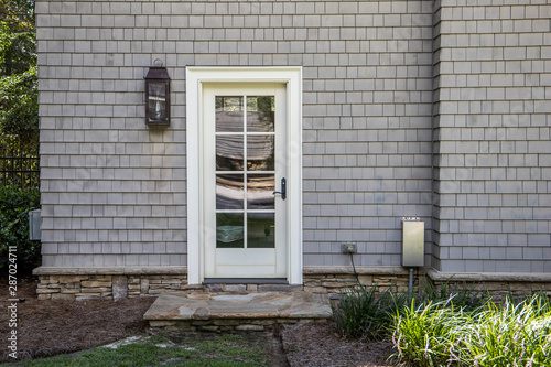 cape cod style home with white wood door at back entrance. Door has many glass windows and outside is an exterior light photo