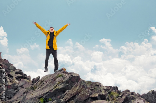 A man with his arms raised in a jump on the background of mountains.
