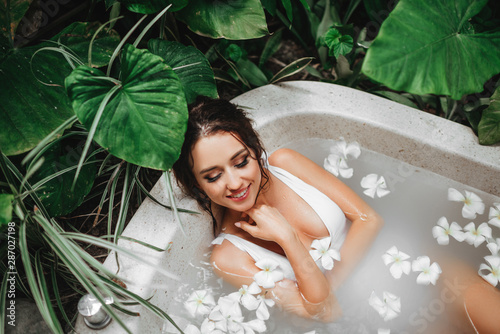 Woman relaxing in round outdoor bath with tropical flowers, organic skin care, luxury spa hotel, lifestyle photo.