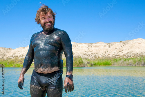 Happy man with healing mud on his skin.