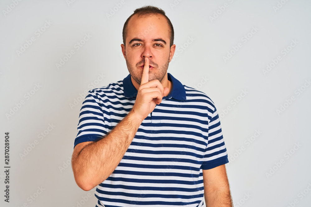 Young man wearing casual striped polo standing over isolated white background asking to be quiet with finger on lips. Silence and secret concept. Young man wearing casual striped polo standing over isolated white background asking to be quiet with finger on lips. Silence and secret concept.