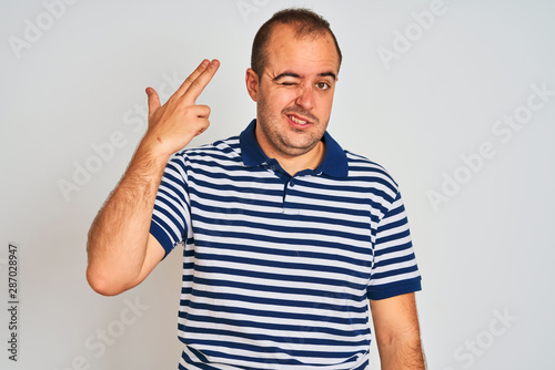 Young man wearing casual striped polo standing over isolated white background Shooting and killing oneself pointing hand and fingers to head like gun, suicide gesture.