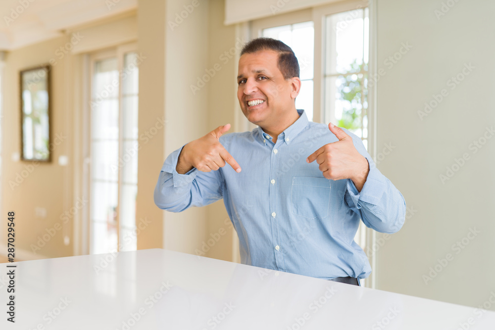 Middle age man sitting at home looking confident with smile on face, pointing oneself with fingers proud and happy.