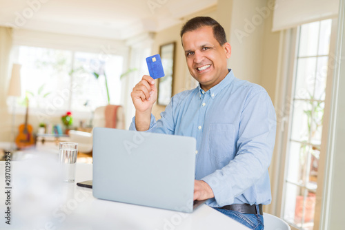 Middle age man showing credit card while using laptop