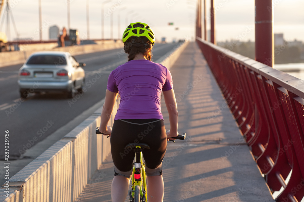 Obraz premium Female cyclist moving forward on big bridge at sunset