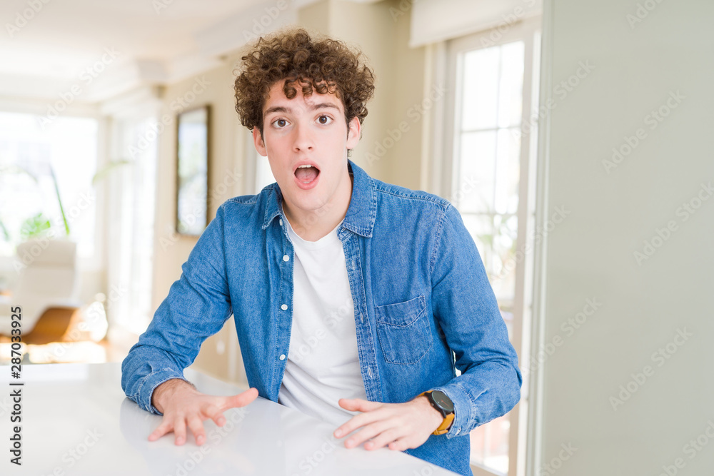 Young handsome man wearing casual denim jacket at home afraid and shocked with surprise expression, fear and excited face.