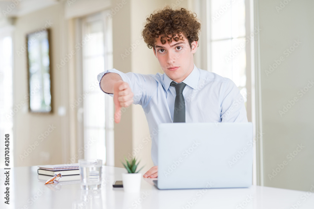 Young business man working with computer laptop at the office looking unhappy and angry showing rejection and negative with thumbs down gesture. Bad expression.